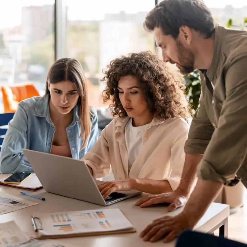 three team members gathered around a table looking at a laptop